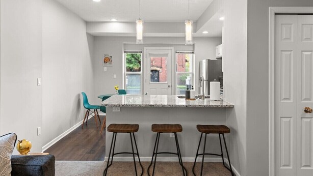 Uma cozinha moderna com bancada de mármore, banquetas, luminárias pendentes e vista para o exterior.