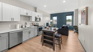 A modern kitchen with white cabinets, a central island, and a dining area with a gray sofa and a chair.