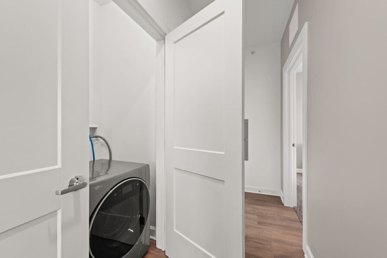 A laundry room with a washing machine, a door, and a hallway leading to another room.