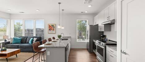 A modern kitchen with a central island, stainless steel appliances, and a dining area with a sofa and chairs.
