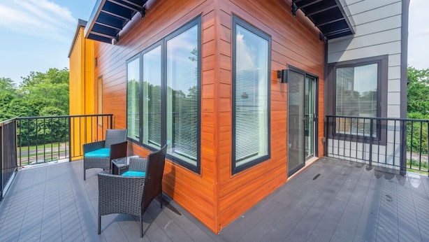 A modern building with large windows, a balcony with wicker furniture, and a view of greenery. - Gorgeous 2 Bed/2 Bath | CLE Clinic | Balcony (Cleveland)