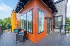 Un edificio moderno con ventanas amplias, un balcón con mobiliario de mimbre y vistas al verdor.