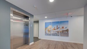 An elevator, a hallway with wooden flooring, and a wall with a cityscape mural. - Gorgeous 2 Bed/2 Bath | CLE Clinic | Balcony (Cleveland)