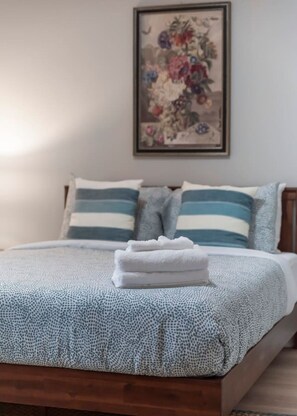 Un lit bien fait, recouvert d’une couvre-lit à motifs, avec deux oreillers à rayures et une œuvre d’art florale encadrée accrochée au mur.