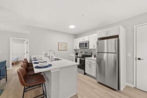 Uma cozinha moderna com armários brancos, eletrodomésticos de aço inoxidável e uma ilha central com banquetas.