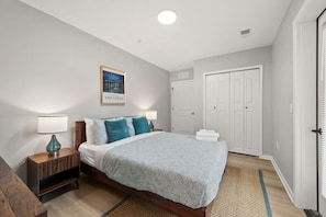 Quarto com cama, mesas de cabeceira, abajur, quadro emoldurado e guarda-roupa.