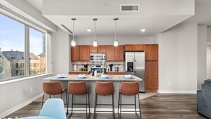 A modern kitchen with a central island, bar stools, and a view of the city through large windows.