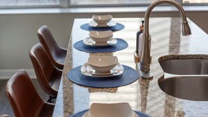 A kitchen with a granite countertop, a stainless steel sink, and a set of brown leather chairs.