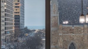 A dining area with a view of a cityscape through a large window, including a tall building and a historic stone building.