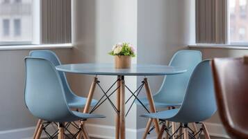 A modern dining area with a round glass table, four blue chairs, and a small potted plant.