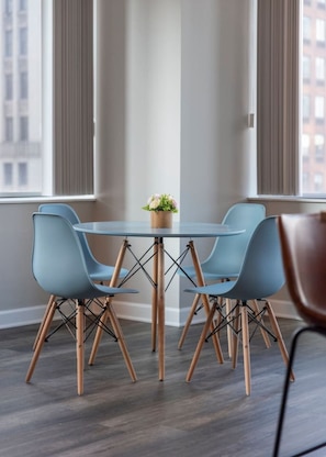 A modern dining area with a round glass table, four blue chairs, and a small potted plant.