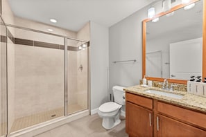 A modern bathroom with a glass shower enclosure, a toilet, a sink with a granite countertop, and a large mirror.