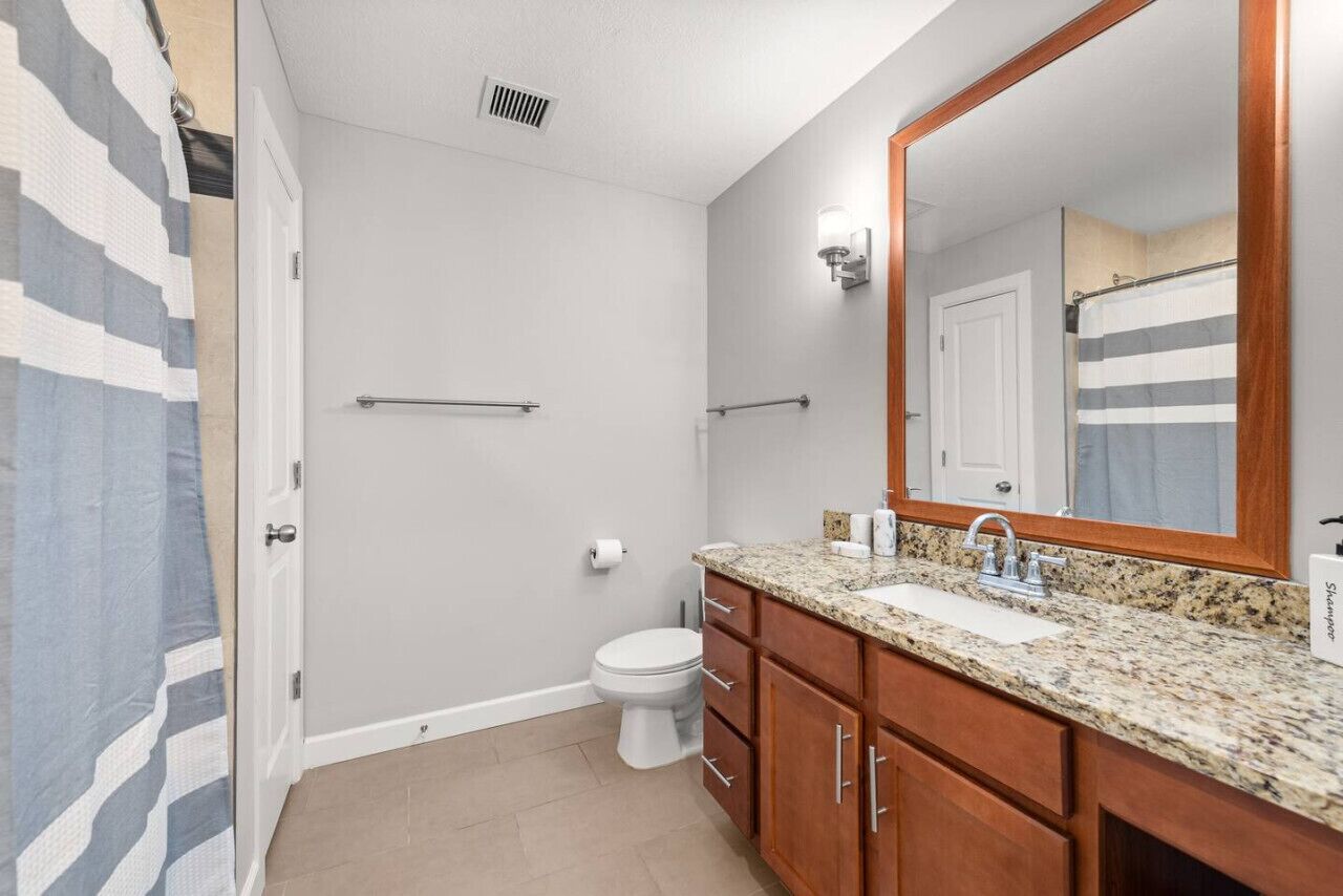 A bathroom with a toilet, sink, mirror, and shower.