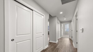 Un pasillo con puertas blancas, piso de madera e iluminación empotrada en el techo.