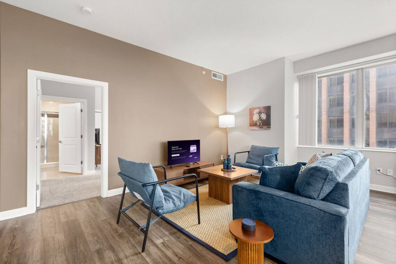 Un salon moderne comprenant un canapé, un fauteuil, une table basse et un téléviseur à écran plat.