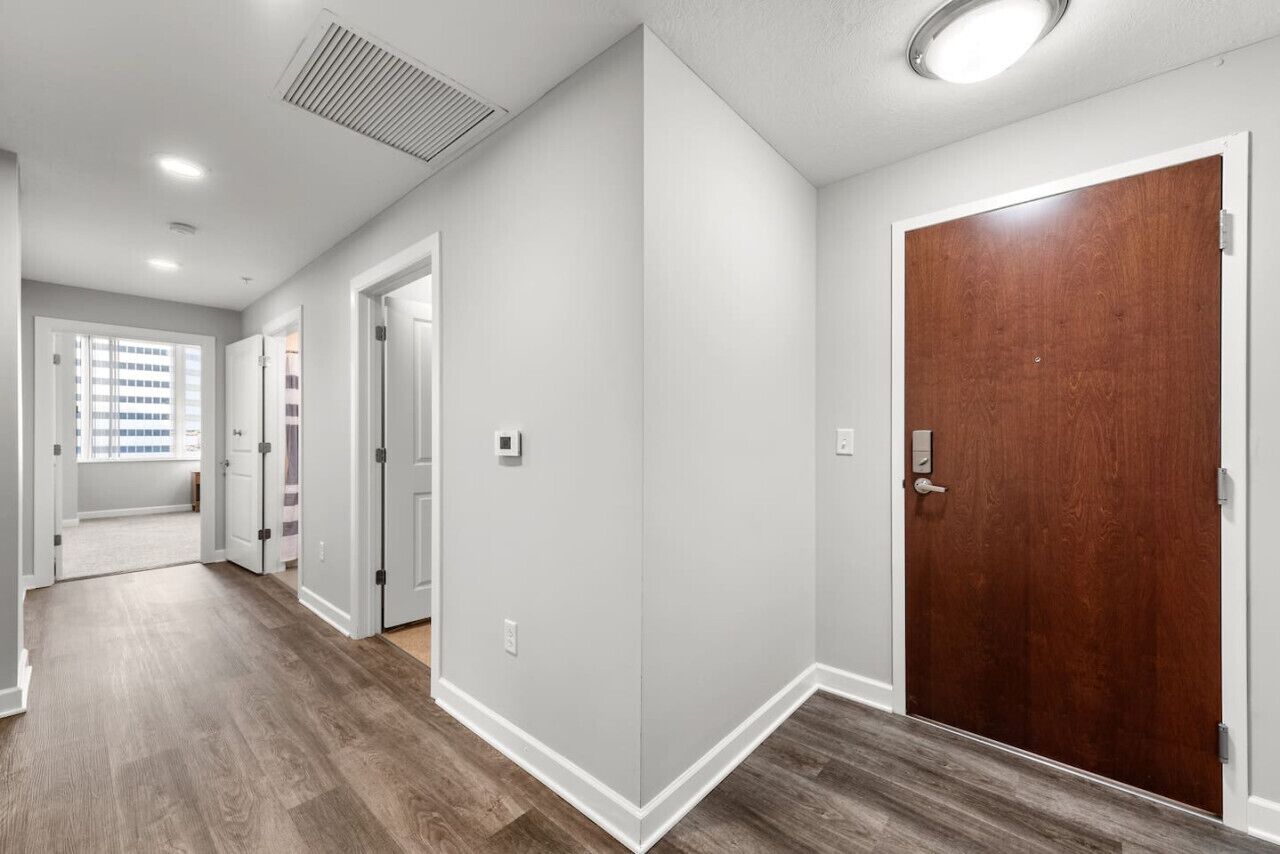 A hallway with wooden flooring, white walls, and a wooden door.