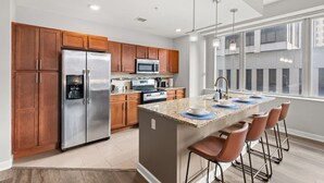 A modern kitchen with wooden cabinets, stainless steel appliances, a granite countertop island, and a bar stool seating area.