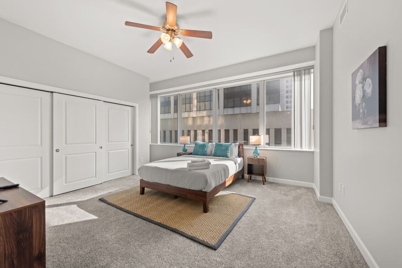 Une chambre à coucher avec un lit, un ventilateur de plafond, une fenêtre et une porte.