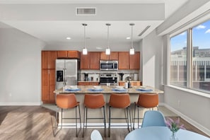 A modern kitchen with wooden cabinets, stainless steel appliances, and a bar area with stools.
