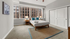 A bedroom with a large window, a ceiling fan, a bed, bedside tables, and a door.