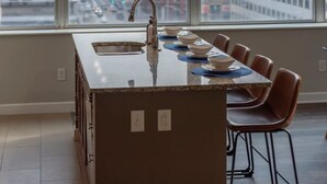 A modern kitchen with a large window, a central island, and a dining area with chairs.