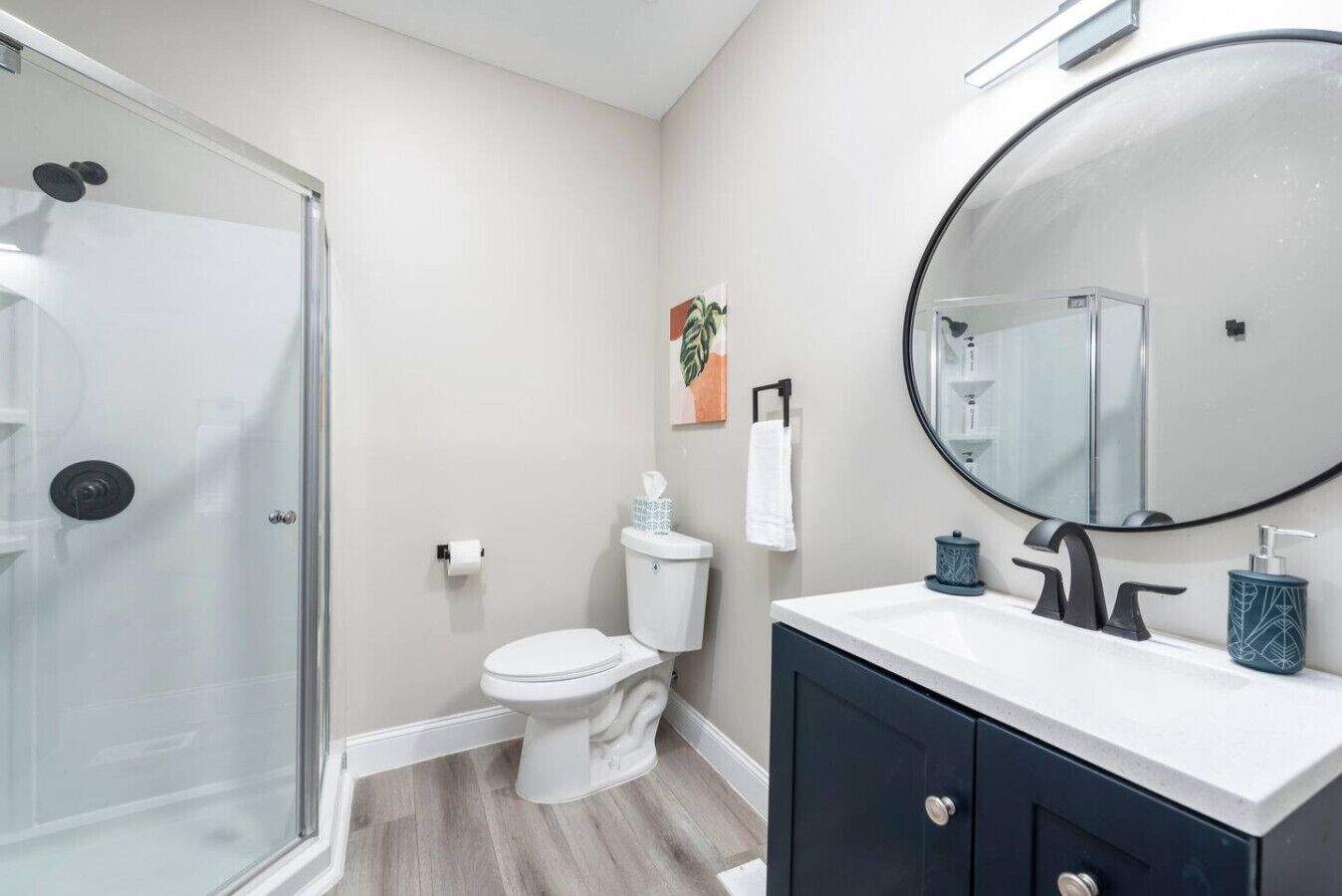 Ein Badezimmer mit Duschkabine aus Glas, Toilette, Waschbecken mit Spiegel und Schrank.