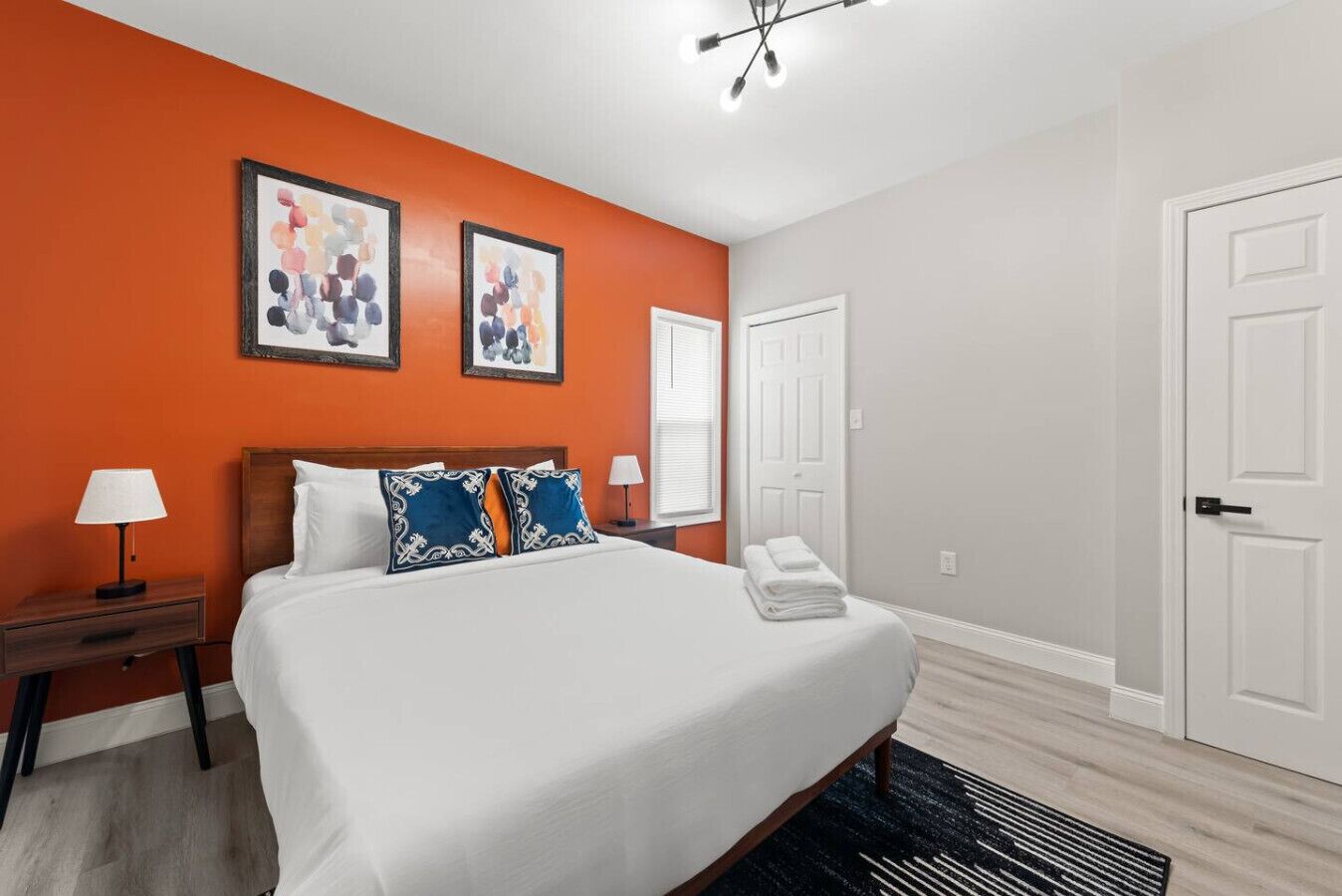 A hotel room with a large bed, two framed artworks on the wall, a nightstand with a lamp, and a door.
