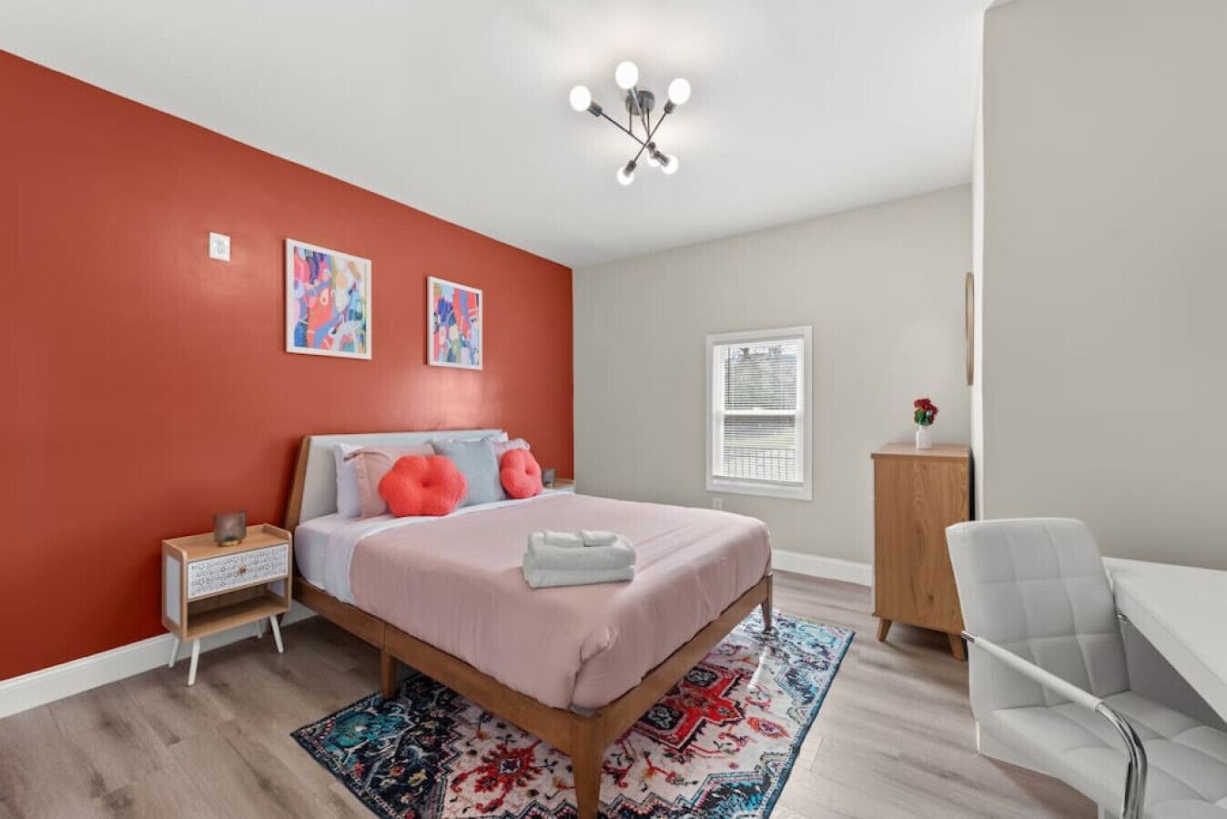 Une chambre à coucher comprenant un lit, une table de chevet, un bureau, une chaise, un tapis et une fenêtre avec des stores.