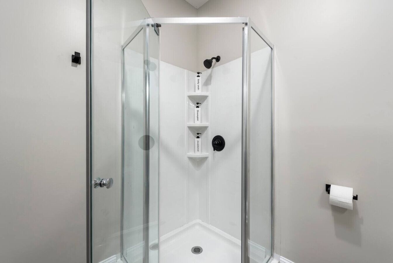 Een douche met glazen wanden, een witte binnenkant, een zwarte douchekop en een witte zeepdispenser.