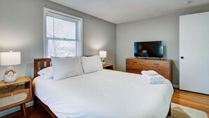A bedroom with a bed, bedside tables, a TV, and a window.