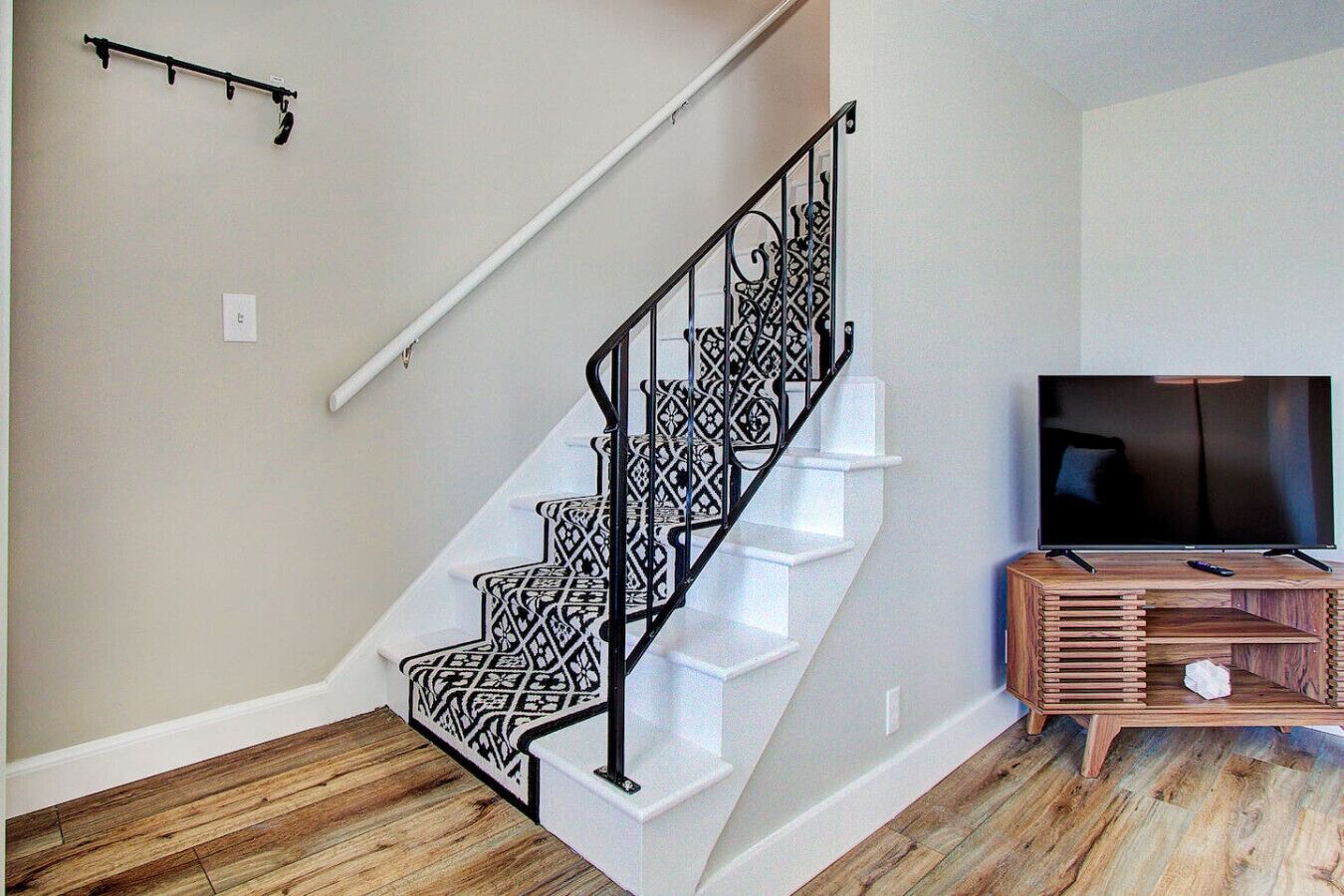 A staircase with a patterned railing, a flat-screen TV on a wooden stand, and a wooden floor.