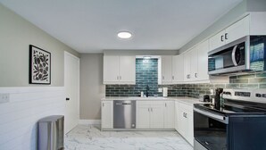 A modern kitchen with white cabinets, a stainless steel dishwasher, a black oven, and a tiled backsplash.