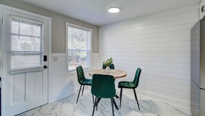 A room with a round table, two chairs, a potted plant, and a door with blinds.