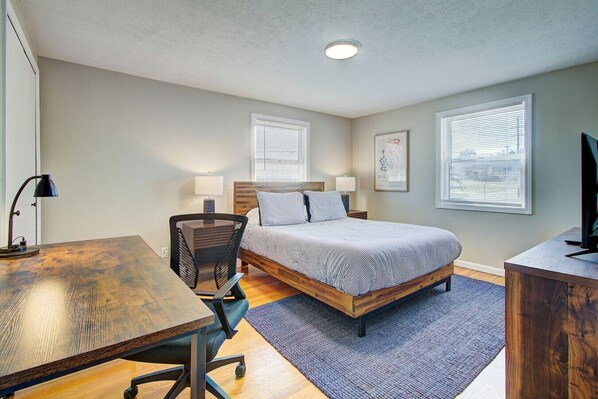 A bedroom with a bed, desk, chair, and a television.