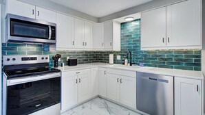 A modern kitchen with white cabinets, a stainless steel microwave, oven, and dishwasher, and a backsplash with green tiles. - Cozy 2BR with Garage | Central North Canton (North Canton)