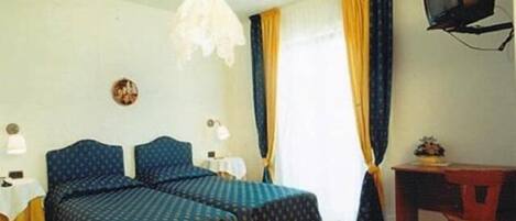 Una habitación con dos camas, un escritorio, un televisor y una ventana con cortinas.