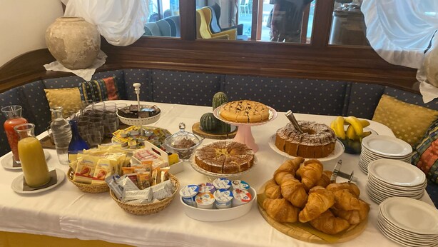 A buffet table with various food items and beverages, a vase, and a window view. - BikeHotel Abete (San Giovanni Rotondo)