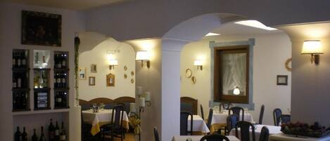 A restaurant with tables set for dining, a wine display, and a fireplace.