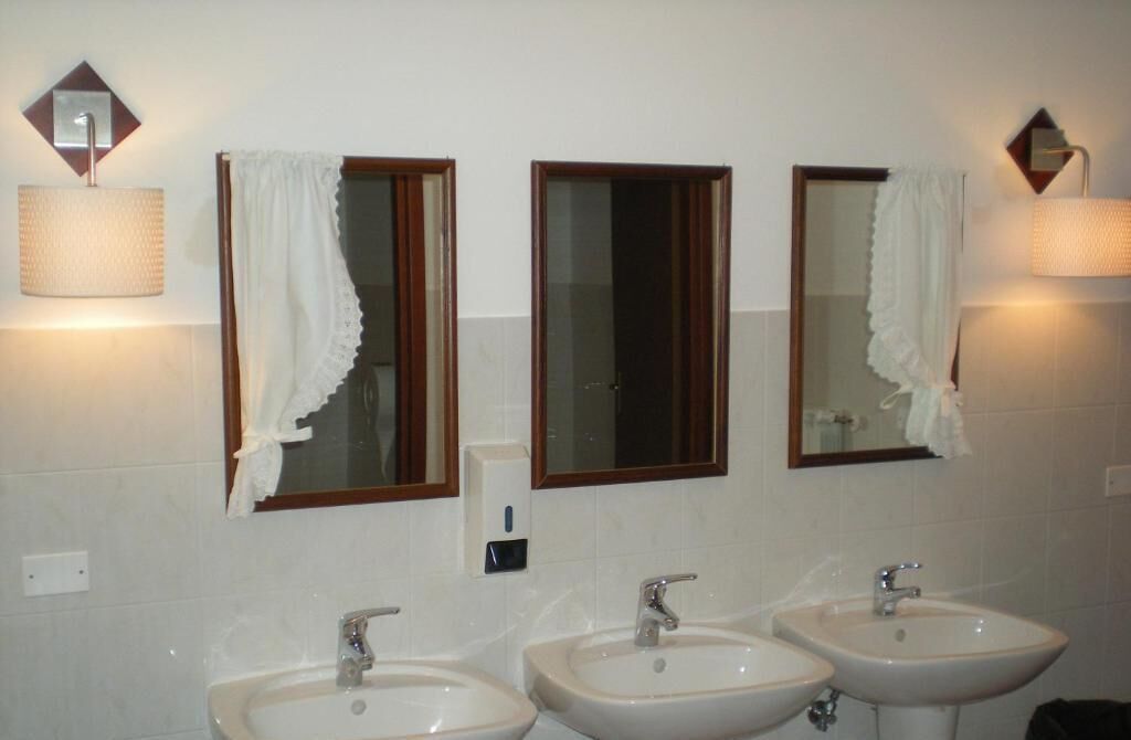 A bathroom with three sinks, two wall-mounted mirrors, and two wall-mounted lamps.