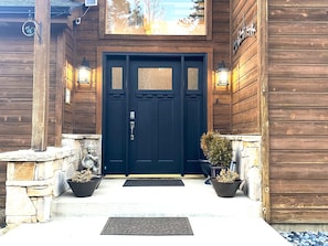 A wooden building with a dark blue door, stone pillars, and two potted plants.