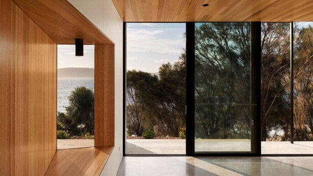 Een modern interieur met houten lambrisering, grote glazen deuren en uitzicht op het omliggende landschap.