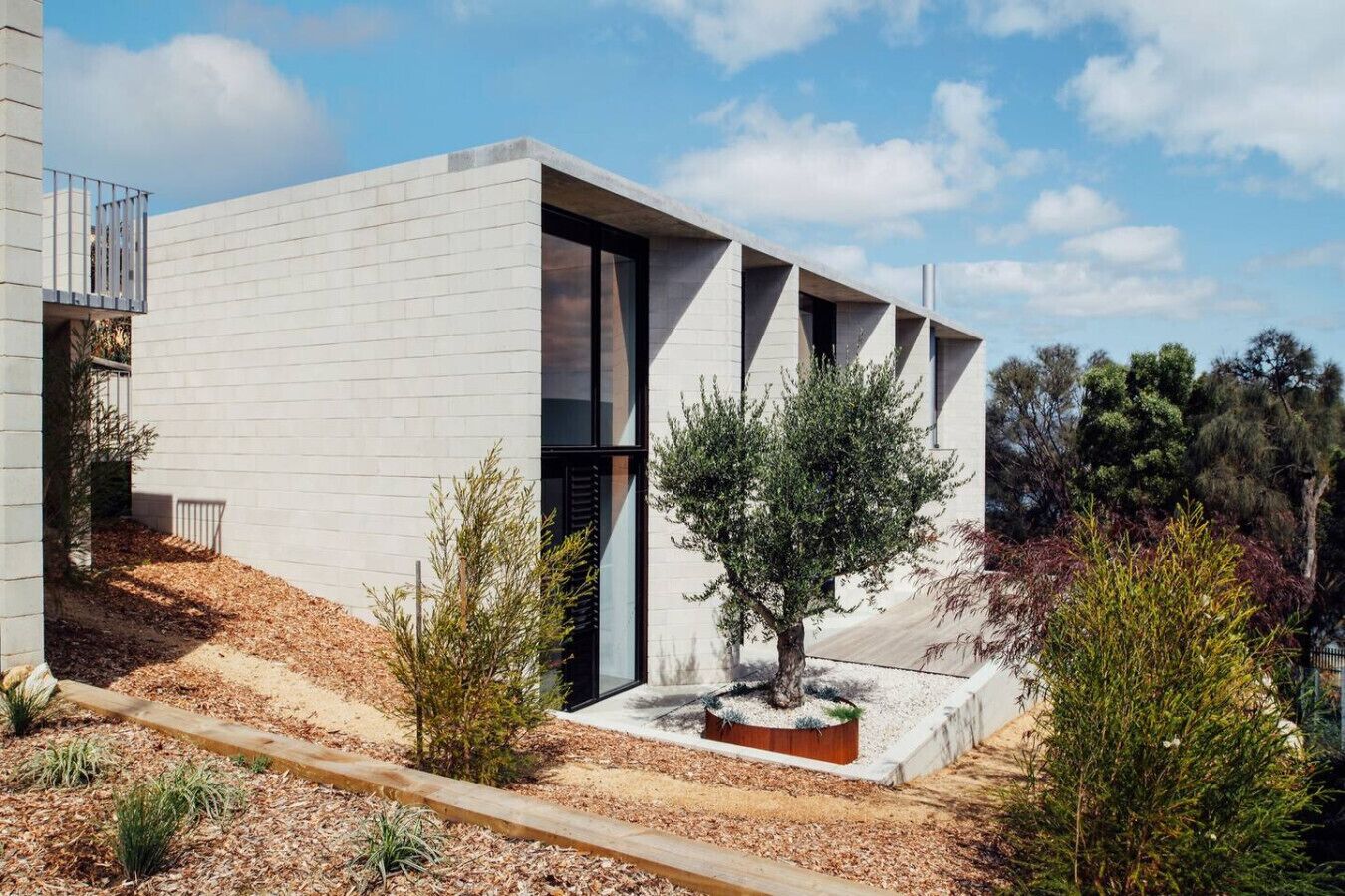 Un edificio moderno con techo plano, ventanas amplias y un pequeño árbol en el jardín delantero.