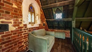 Une pièce mansardée chaleureuse avec des murs en briques apparentes, un plafond en bois et une petite fenêtre ornée de vitraux.