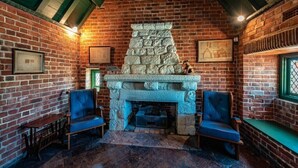 Une pièce chaleureuse avec une cheminée en pierre, deux fauteuils bleus confortables et un mur de briques orné de tableaux encadrés.