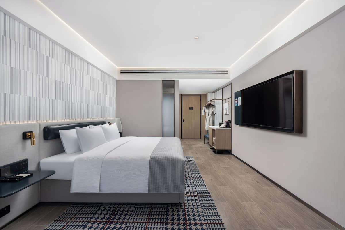 Quarto de hotel moderno com uma cama grande, televisão de tela plana, mesa de cabeceira e guarda-roupa.