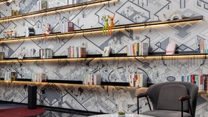 Una biblioteca moderna con paredes de diseño geométrico, estanterías y una mesa redonda con una planta.