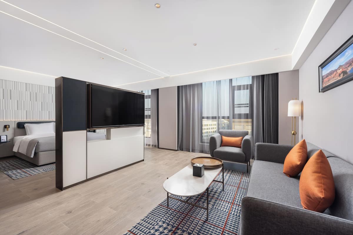 Quarto de hotel moderno com uma cama grande, um sofá, uma TV e vista para a cidade.