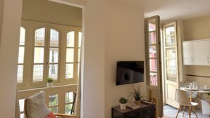 Ein Zimmer mit großem Fenster, Fernseher, Esstisch mit Stühlen und einem Schrank.