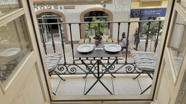 Ein Balkon mit zwei Tischen, jeder Tisch mit einem Teller und einem Glas, sowie einem Stuhl.