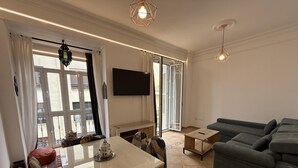 A modern living room with a sofa, a TV, a dining table, and a patterned rug.
